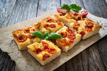 Focaccia - baked sandwich with tomatoes and basil leaves on wooden table