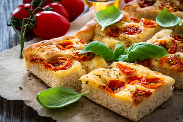 Focaccia - baked sandwich with tomatoes and basil leaves on wooden table