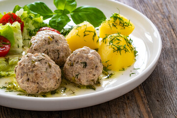 Cooked meatballs in dill sauce with boiled potatoes and fresh vegetables on wooden table
