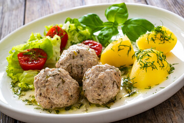 Cooked meatballs in dill sauce with boiled potatoes and fresh vegetables on wooden table
