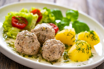 Cooked meatballs in dill sauce with boiled potatoes and fresh vegetables on wooden table
