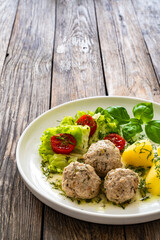 Cooked meatballs in dill sauce with boiled potatoes and fresh vegetables on wooden table
