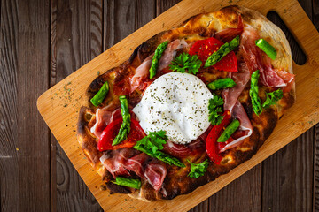Roman Pinsa with burrata cheese, ripened ham and green asparagus on wooden table
