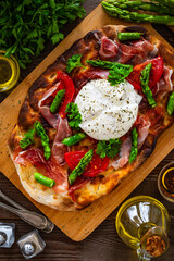 Roman Pinsa with burrata cheese, ripened ham and green asparagus on wooden table
