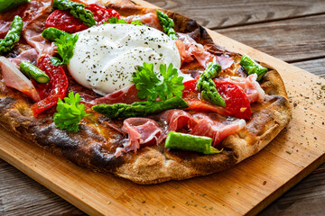 Roman Pinsa with burrata cheese, ripened ham and green asparagus on wooden table
