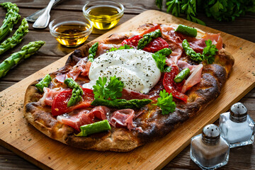 Roman Pinsa with burrata cheese, ripened ham and green asparagus on wooden table
