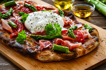 Roman Pinsa with burrata cheese, ripened ham and green asparagus on wooden table
