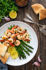 Fried shrimps with garlic and parsley in olive oil and cooked green asparagus on wooden table
