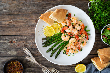 Fried shrimps with garlic and parsley in olive oil and cooked green asparagus on wooden table
