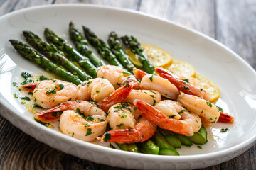 Fried shrimps with garlic and parsley in olive oil and cooked green asparagus on wooden table
