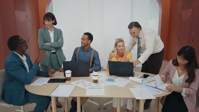 People working together in modern start up office. Multiethnic women and men planning and working on the company future projects. Business team sitting at the table and discussing new marketing ideas.