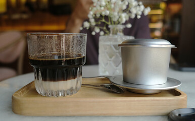 Close-up of a glass of Vietnamese coffee with a metal filter on a wooden tray in a café in Hoi An, Vietnam, capturing the essence of traditional coffee preparation