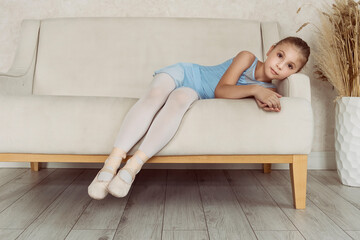 portrait of a ballerina girl in a blue bodysuit and skirts lying on the back of the sofa