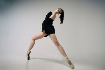 ballerina in a bodysuit and a black jacket improvises classical and modern choreography in a photo...