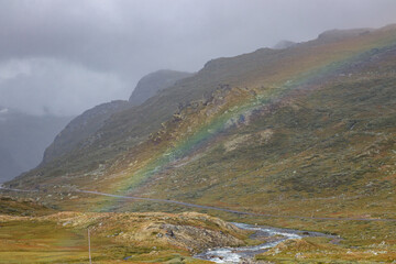 Colorful rainbow on a cloudy day. Sognefjellsvegen winding through the mountains of Jotunheimen National Park. Norway.