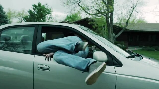 Back shot of a young Caucasian man running and jumping into a moving car through the window