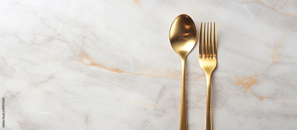 Aufkleber design concept with clean golden metal cutlery on a light marble background in a top view copy space