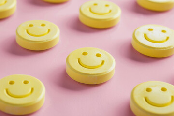 A row of yellow pills with smiling faces on them. The pills are arranged in a pattern, with some overlapping and others standing alone. Scene is cheerful and lighthearted
