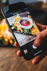 close-up hand holding a smartphone, capturing a colorful dish with garnishes. smartphone screen displays the meal being photographed, highlighting the modern trend of documenting culinary experiences