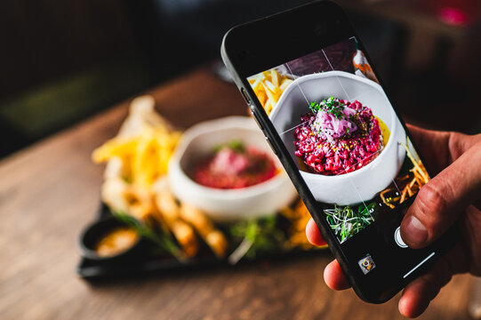 close-up hand holding a smartphone, capturing a colorful dish with garnishes. smartphone screen displays the meal being photographed, highlighting the modern trend of documenting culinary experiences