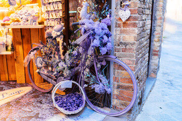bicycle decorated with purple flowers and ribbons outside shop with brick wall