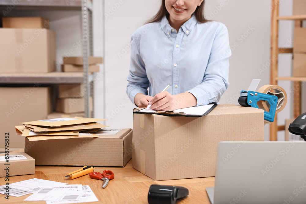 Wall mural Parcel packing. Post office worker with clipboard writing notes at wooden table indoors, closeup