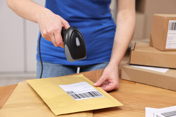 Parcel packing. Post office worker with scanner reading barcode at wooden table indoors, closeup