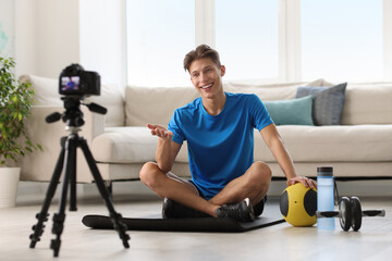 Smiling sports blogger recording fitness lesson with camera at home