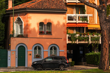 colorful suburban houses with red tiled roofs, lush greenery, and a parked car, under bright sunlight