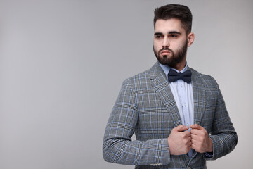 Portrait of handsome man in suit, shirt and bow tie on grey background. Space for text