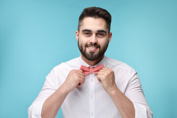 Smiling man in shirt adjusting bow tie on light blue background