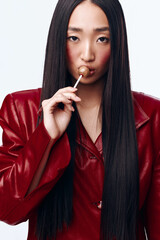 Stylish Asian woman with long black hair wearing red jacket holding piece of candy in mouth