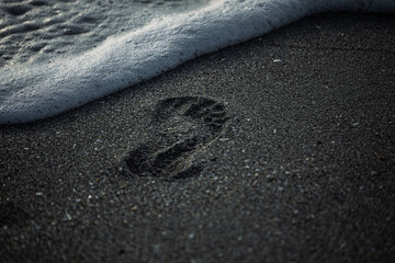a photo of someones footprints in the sand and a wave