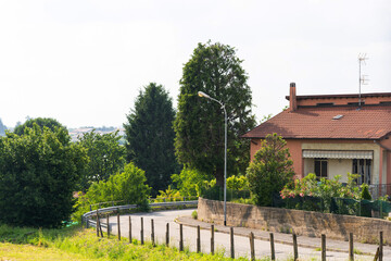 suburban house with red roof, surrounded by lush greenery and a winding road, under a bright sky