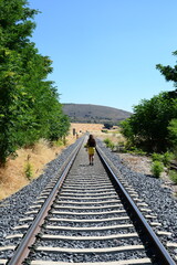 Fototapeta premium Young woman walks thoughtfully along the railroad tracks through the countryside