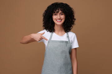 Happy woman pointing at kitchen apron on brown background. Mockup for design
