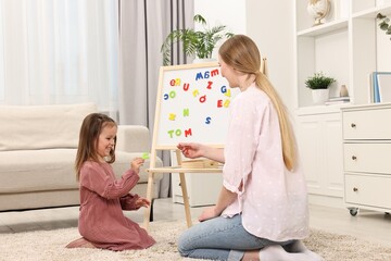 Mom teaching her daughter alphabet with magnetic letters at home