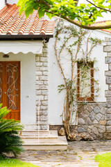 front entrance of a charming house with wooden doors, stone pillars, and lush green plants
