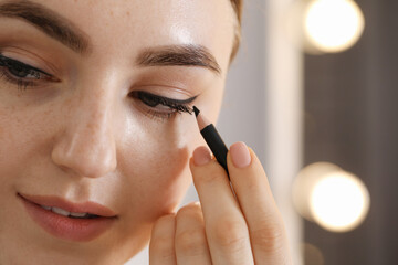 Makeup product. Woman applying black eyeliner indoors, closeup