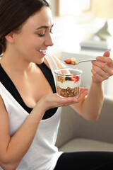 Woman eating tasty granola with fresh berries and yogurt at home