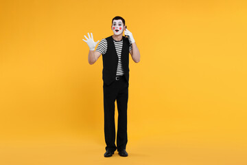 Funny mime artist talking on phone against orange background