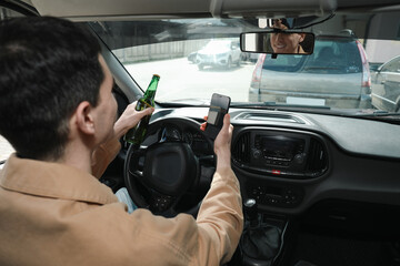 Man with bottle of beer and smartphone in car. Don't drink and drive concept