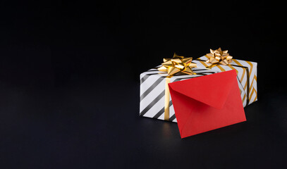 striped gift box with gold bow and red envelope on black background, holiday theme