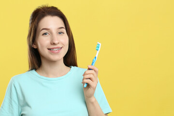 Portrait of smiling woman with dental braces and toothbrush on yellow background. Space for text