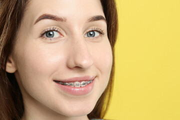 Portrait of smiling woman with dental braces on yellow background, closeup