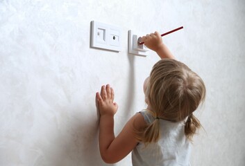 Little child playing with electrical socket and pencil indoors, space for text. Dangerous situation