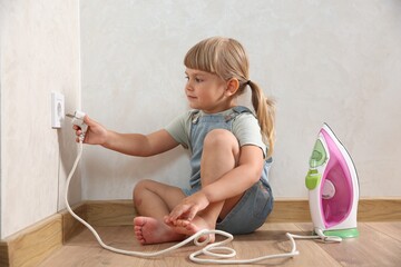 Little child playing with electrical socket and iron plug at home. Dangerous situation