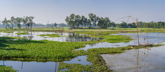 Scenic rural landscape panorama with wooden boats and traditional chinese fishing nets in Tangail countryside, Bangladesh	