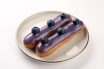 Delicious eclairs decorated with blueberries on white background