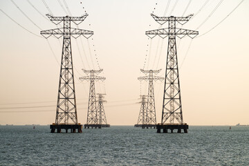 High voltage transmission towers over sea water in sunset